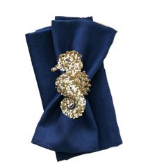 a blue napkin with gold sequins and a seahorse brooch on it