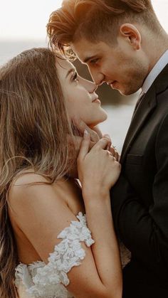 a man and woman standing next to each other in front of the ocean with their arms around each other