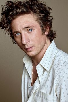 a man with curly hair and blue eyes posing for a photo in a white shirt