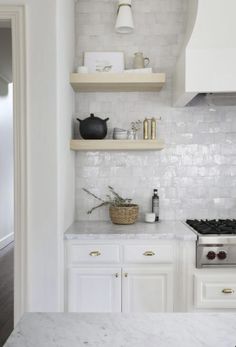 a white kitchen with marble counter tops and shelves above the stove, along with an open shelf