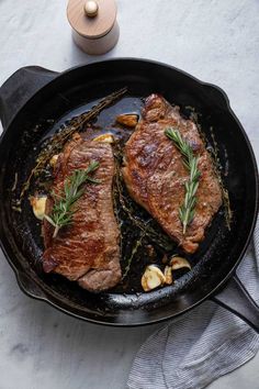 two steaks cooking in a skillet with herbs and garlic on the side, ready to be cooked