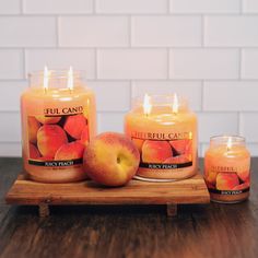 three candles sitting on top of a wooden tray filled with apples next to each other