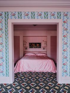 a pink bed sitting in the middle of a bedroom next to a wall with flowers on it