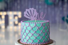 there is a cake that has been decorated with mermaid scales and a purple crown on top