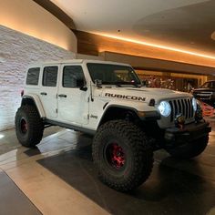 a white jeep is parked in front of a large wall and some people are looking at it