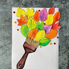 an art project made out of paper and colored leaves on a white sheet with a brown brush