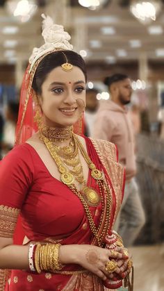 a woman in a red and gold bridal outfit smiles at the camera while standing with other people