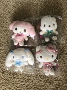 four hello kitty stuffed animals in plastic bags on the floor next to a carpeted area