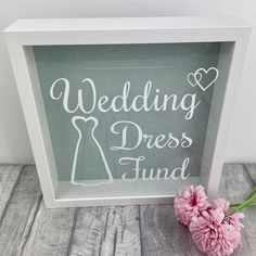 a pink flower sitting next to a white frame with the words wedding dress fund written on it