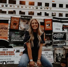 a woman sitting on the back of a food truck with posters behind her in front of it