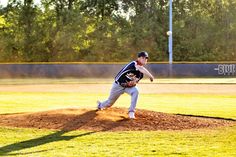 a baseball player pitching a ball on top of a field in front of trees and grass