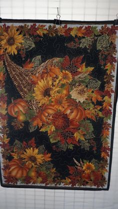 a quilt hanging on the wall with fall leaves and sunflowers in front of it