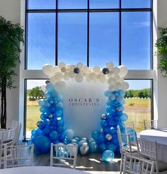 an entrance decorated with blue and white balloons in front of a large window, surrounded by chairs