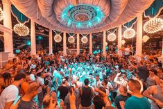 a large group of people dancing in a room with lights on the ceiling and curtains