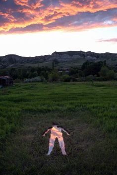 a reflection of a person in the grass with mountains in the backgrouds