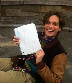 a man sitting on the ground holding up a notebook