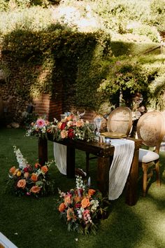 an outdoor table with flowers and greenery on the grass, surrounded by wicker chairs