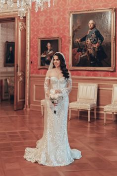 a woman in a wedding dress standing in a room with paintings and chandeliers