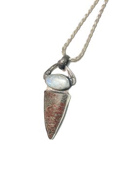 a silver necklace with an arrow shaped pendant on it's end and a stone in the middle