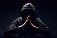 a man in a hoodie is sitting at a table with his hands folded over his face