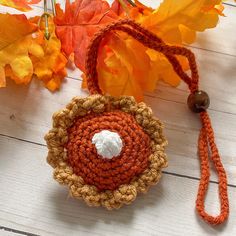 an orange and brown crocheted flower on a white wooden table with autumn leaves