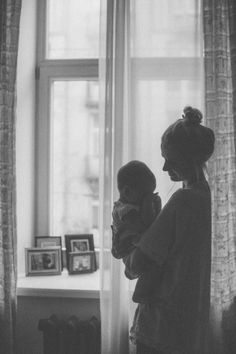 a woman standing in front of a window holding a baby