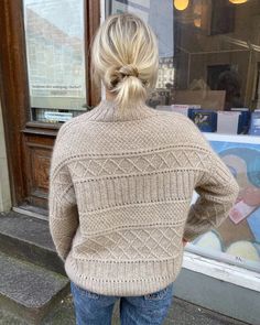 a woman standing on the sidewalk in front of a store window with her back to the camera