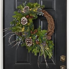 a wreath with pine cones and evergreens on the front door is lit by christmas lights