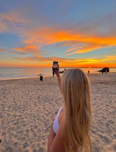 a woman on the beach taking a photo with her cell phone at sunset or dawn