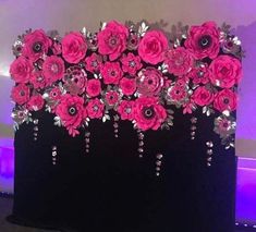 pink flowers are on display in front of a purple wall and black table cloth with silver sequins