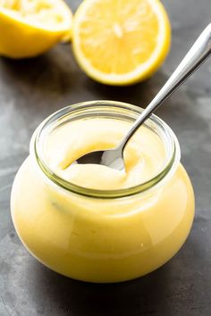 a glass jar filled with lemon custard on top of a black table next to sliced lemons