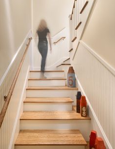 a person walking up some stairs in a house with white walls and wooden steps leading to the second floor