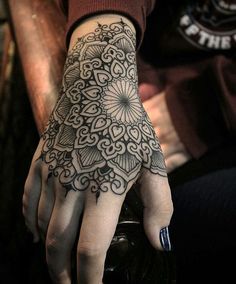 a person's hand with a tattoo on it, and the other hand has an intricate