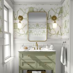 a bathroom with green vanity and wallpaper on the walls, along with a gold framed mirror