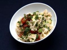 a white bowl filled with pasta and vegetables on top of a blue tablecloth next to a fork