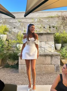 a woman in a short white dress standing under an umbrella