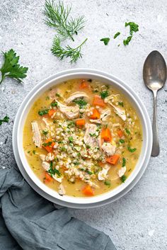 a white bowl filled with chicken and rice soup next to a spoon on a gray surface