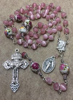 "This beautiful handmade rosary is made with 8mm cat's eye matte pink glass, 10mm ceramic beads and 2\" Pardon crucifix. Length: 20\" inches long" Pretty Rosaries, Rosary Prayers Catholic, Flower Rosary, Personalized Rosary, Handmade Rosary, Holy Rosary, Immaculate Conception, Catholic Rosary, Diy Bracelet Designs