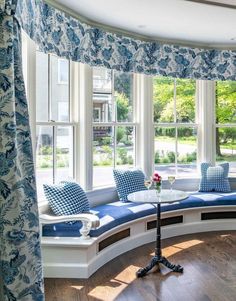 a circular window seat with blue and white pillows on it in front of a bay window