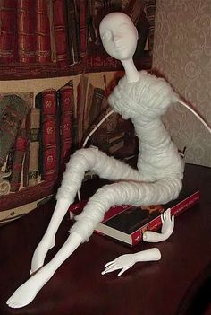 a white mannequin sitting on top of a wooden table next to a book