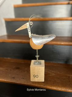 a small metal bird sitting on top of a wooden block in front of some stairs