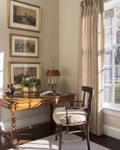 a room with a desk, chair and pictures on the wall above it in front of a window