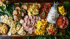 many different types of food are arranged on a wooden platter with green leaves and flowers