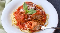 a white plate topped with spaghetti and meatballs covered in marinara sauce, parmesan cheese and basil