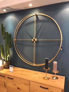 a large clock on the wall next to a wooden dresser with candles and cacti