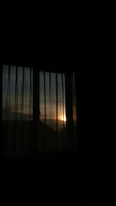 the sun is setting through some curtains