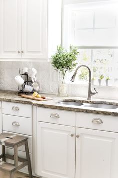 a kitchen with white cabinets and marble counter tops