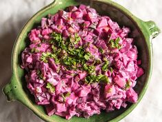 a green bowl filled with food on top of a white tablecloth covered flooring