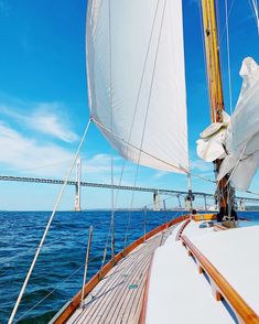 the sailboat is sailing on the open water with a bridge in the back ground