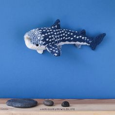 a knitted fish hanging on the wall next to some rocks and a blue background